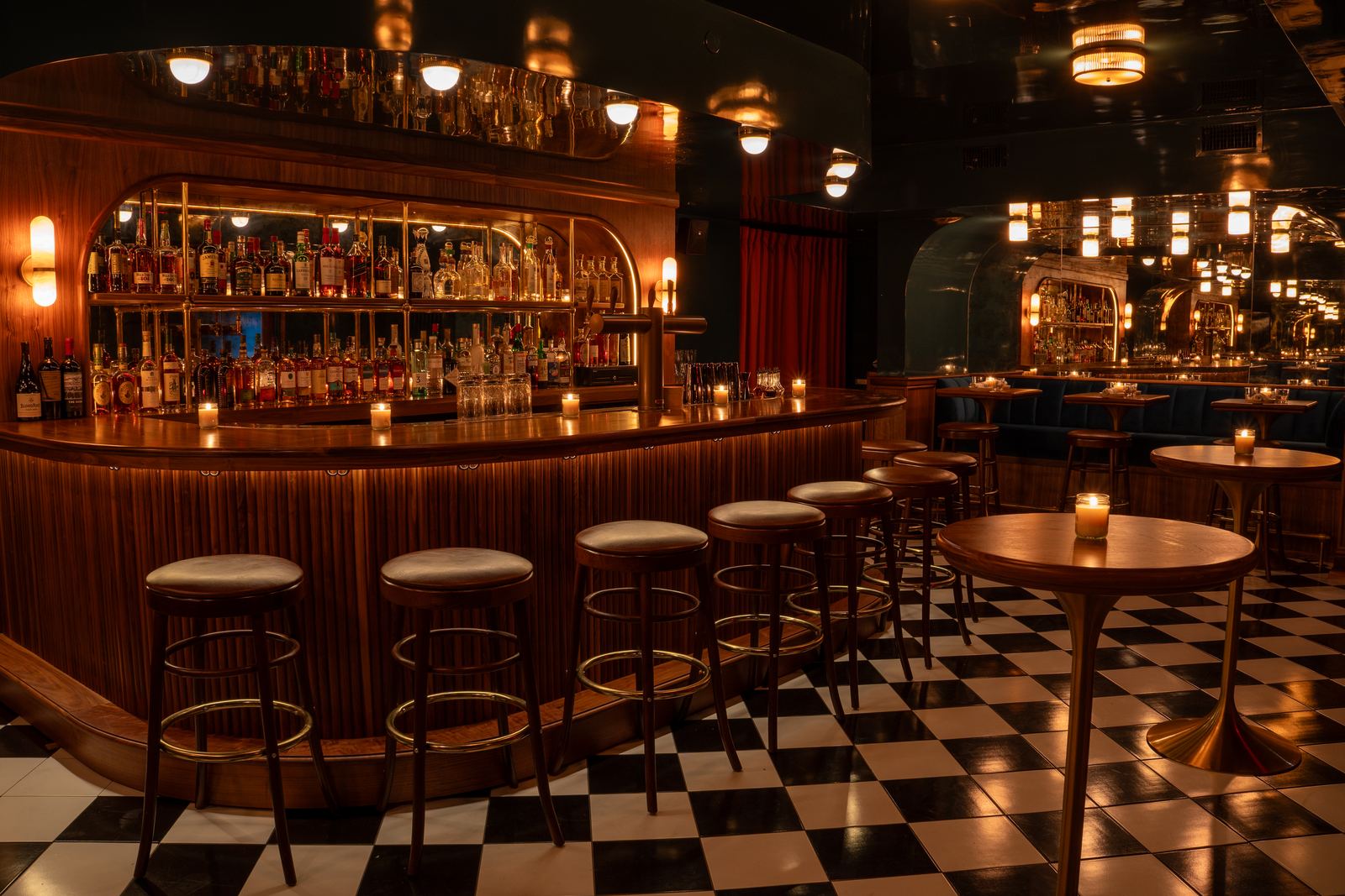 Downstairs — a curved wooden bar with leather stools on a black-and-white checkerboard floor, mirrored ceiling glowing above.